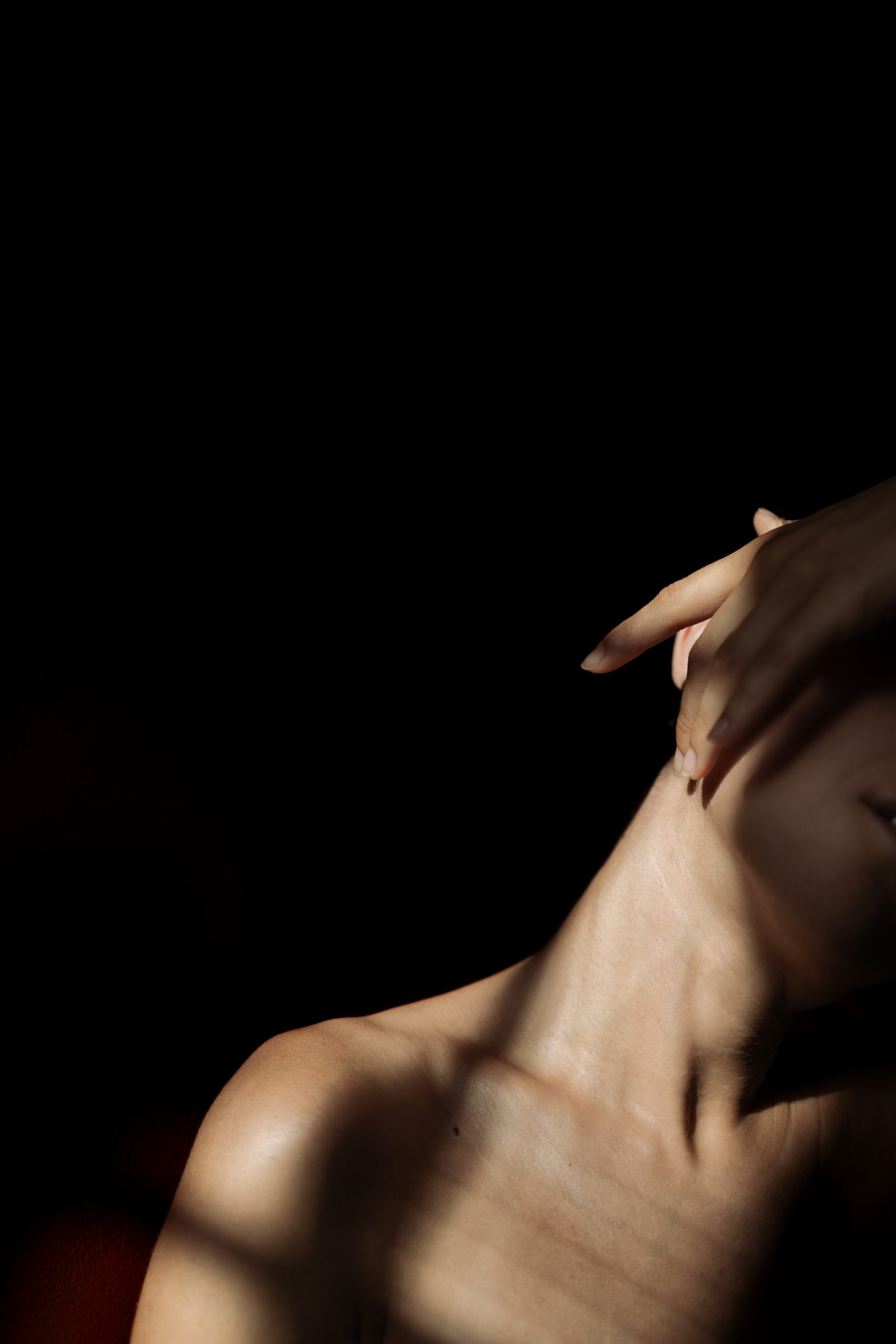 Autoritratto fotografico artistico in primo piano che ritrae spalla, collo e mano con giochi di luce e ombra su sfondo scuro.